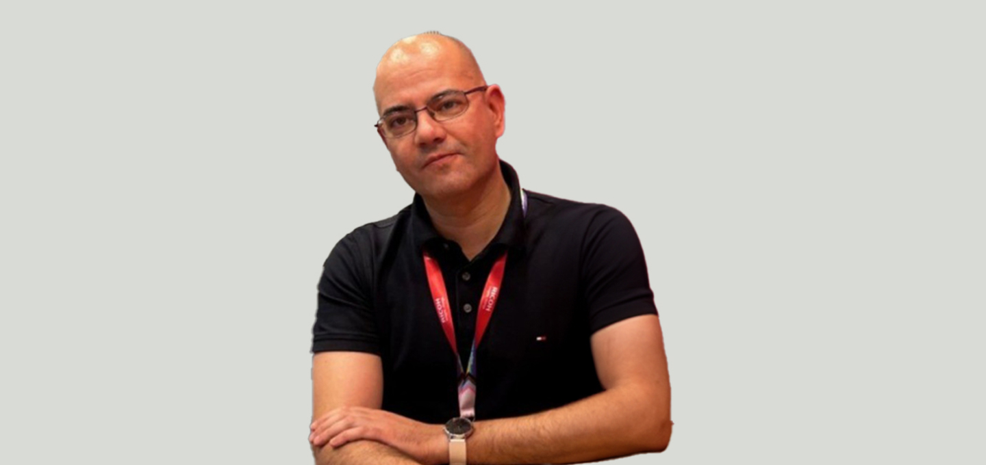 Retrato del ponente Xavier Menendez Oliveros, con polo oscuro y gafas, apoyando los brazos sobre una superficie, con fondo neutro.